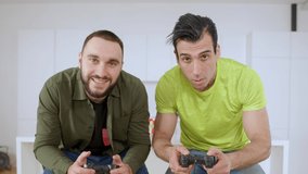 Middle Eastern man losing in video game and leaving as Caucasian guy rejoicing win. Positive relaxed friends enjoying weekend leisure gaming indoors at home. Lifestyle and relaxation.
