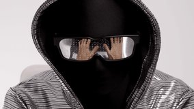 Computer hacker in hooded top and sunglasses typing on keyboard