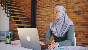 Young Muslim girl in a hijab has a video call with a laptop. Woman designer talks about her project, online design training