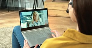 Close up of female patient in headset having online medical consultation with Caucasian senior woman professional doctor on laptop sitting in room. Physician talking on video call, over shoulder view