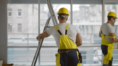 Electrician climbing stepladder doing house renovation. Side view of construction worker in safety helmet and overall using ladder checking wires on ceiling at construction site