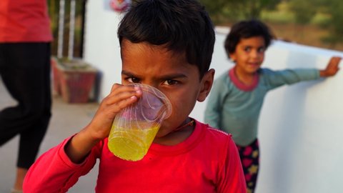 10 March 2021- Reengus, Jaipur, India. Cheerful kid taking lemon fruitee drink in a plastic glass. Red ornamented boy with Lemon juice in hot sunny day.