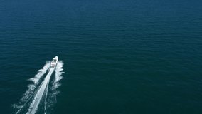 A speedboat of white color in the rays of the sun moves quickly on blue water, top view. Flying over the boat top view. Drone shooting 4k video. Aerial video. Diagonal boat movement on the water.