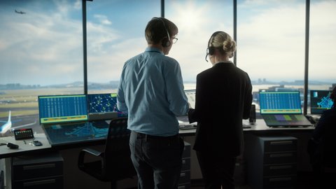 Female and Male Air Traffic Controllers with Headsets Talk in Airport Tower. Office Room is Full of Desktop Computer Displays with Navigation Screens, Airplane Flight Radar Data for the Team.