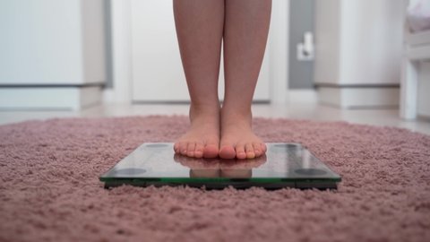 The legs of the child on the scales. A little girl gets bare feet on the scales. Scales on pink carpet. The concept of weight loss and excess weight in children. Good and correct weight for the child