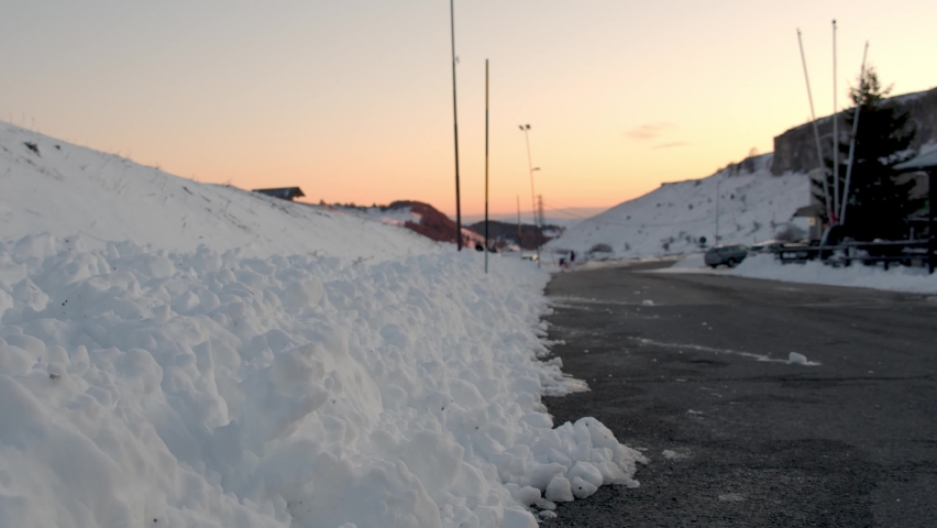 Girl walks on the edge of a snowy road.
Tourist comes home during sunset. End of the day spent in the mountains.