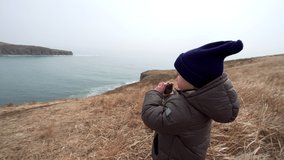 Adorable 4 years old boy is taking photo or video of beautiful marine landscape: blue sea and high shores. Spring.