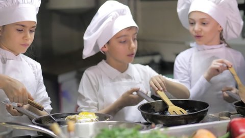 Kids learning how to cook eggs in a cooking class in restaurant kitchen