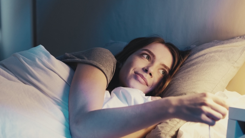 Good night. Sweet dreams. Bedtime rest recreation. Happy relaxed satisfied woman lying down in cozy comfortable bed turning off light falling asleep smiling in dark bedroom with blue moonlight. | Shutterstock HD Video #1069641469