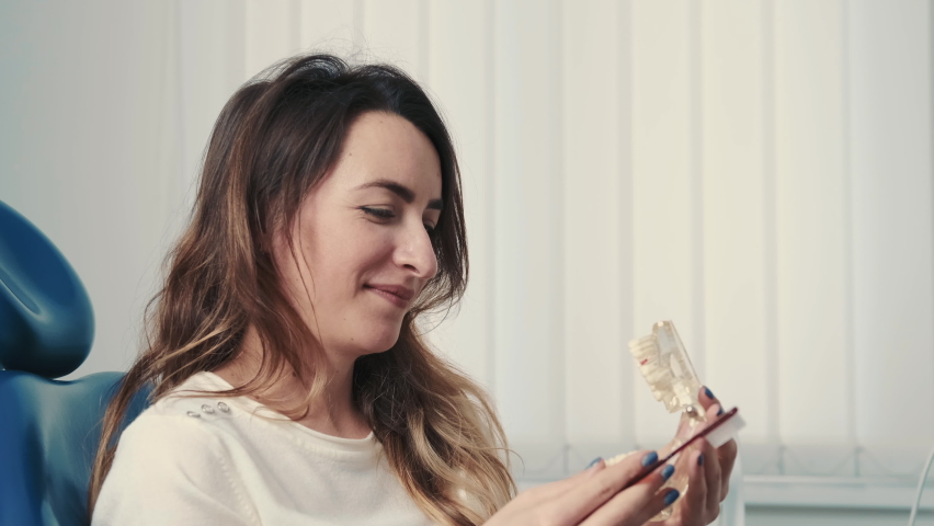 Portrait Of Woman Holding Jaw Model And Toothbrush Sitting At Dentist At Dental Care Consultation Reception
