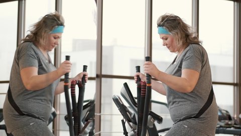 Middle aged overweight woman using ellipse machine at gym