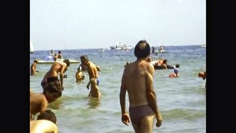 Cesenatico, Italy - circa August 1975: tourists bathing with children in the Adriatic sea waterfront in summer. Bathhouses on the beach of Cesenatico town. Archival of Italy in the 1970s.