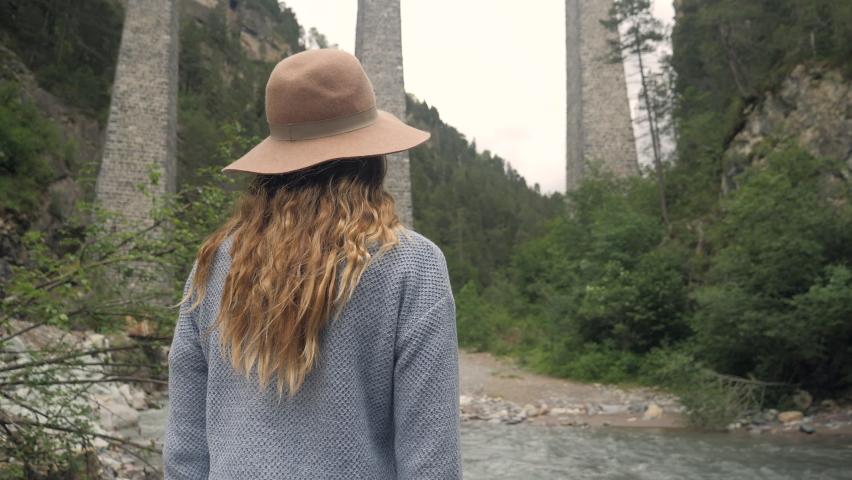 Woman contemplates railroad track viaduct from below 