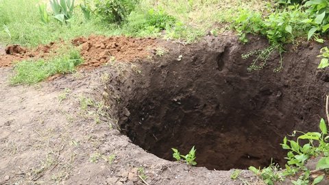 A man digs a deep round pit with a shovel. A man  throws the ground with a shovel.
