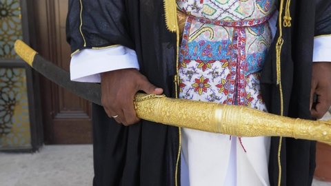 An Omani man in traditional Omani uniforms, holding a sword and wearing an Omani dagger ( khanjar) 