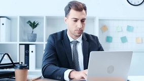 disappointed businessman using laptop while sitting at desk in office