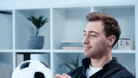 slow motion of cheerful businessman playing with soccer ball while sitting at workplace in office