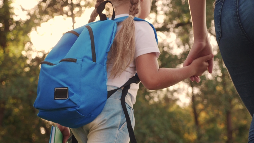 Mom and daughter go to school. happy family education concept. schoolgirl with mom and daughter go hand in hand to school on footpath lifestyle in the park. little girl with a briefcase time to study | Shutterstock HD Video #1069667407