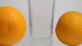 Taste of nature. Super slow motion shot of pouring orange juice into a transparent glass and two oranges against white background. Close up. Healthy drink, vitamins, fruits concept