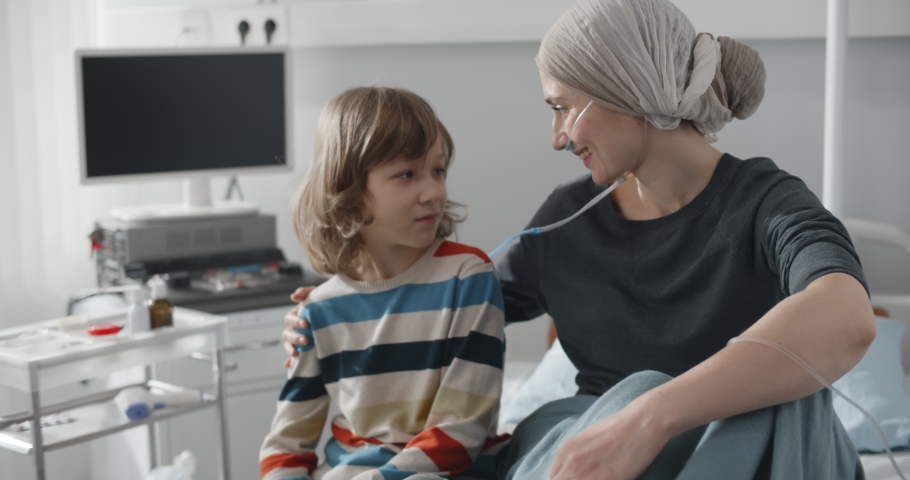 Mother fighting with cancer hugging little son while resting on hospital bed. Boy kid visiting sick mom in cancer clinic sitting together on bed and embracing in hospital ward Royalty-Free Stock Footage #1069670275
