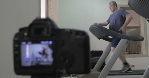 MOSCOW, RUSSIA - April 21, 2015: Digital camera shooting photos or timelapse of a man jogging on treadmill in the gym. Shot with changing focus