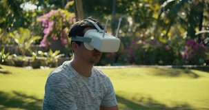 A man in a virtual reality helmet is studying a virtual game. A guy in the park in a gray T-shirt against a background of green trees looks in VR glasses. 4K slow motion.