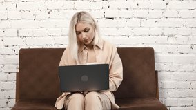 Happy stylish female employee is using laptop, having online conference with colleagues. Attractive business woman sitting on sofa, discussing a project with coworkers, remotely work concept