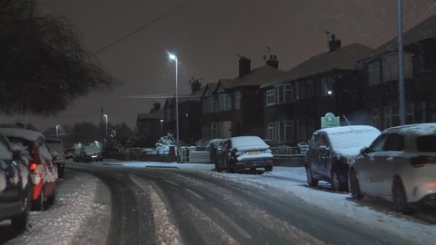 SALFORD, GREATER MANCHESTER, UNITED KINGDOM - CIRCA JANUARY, 2021: Driving at night in winter in residential area. Road, cars, houses covered in snow; not every winter snowing in Northwest of England.