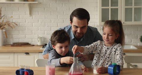 Father and little children spend weekend engaged in playtime in kitchen, play together with science kits adding powder pouring liquids in bulb, making funny chemical experiments at home. Hobby concept
