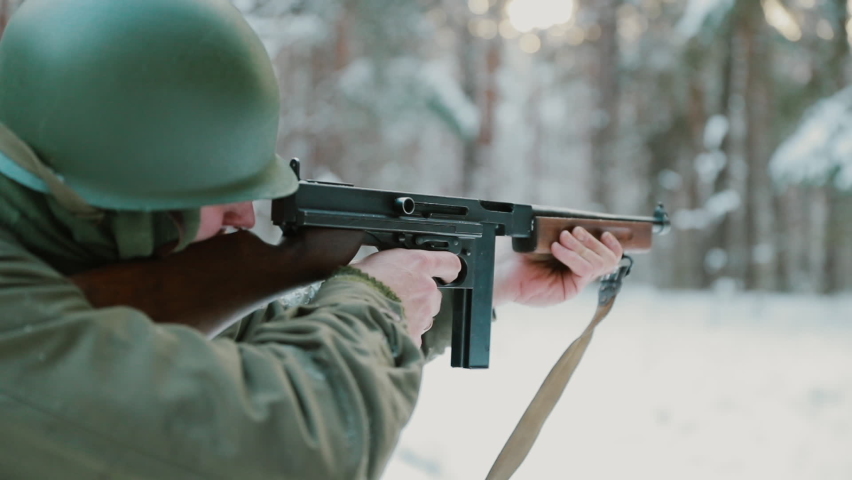 Slow Motion Soldier dressed as USA Infantry Soldier Of World War II Aiming And Shooting From Submachine Gun Weapon. American Soldier In Attack In Winter Forest.