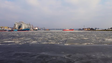 Aerial drone footage of cargo terminal on melting ice with ships and harbor cranes on pier and grain storage tanks. Concept of transport logistics and maritime in winter.