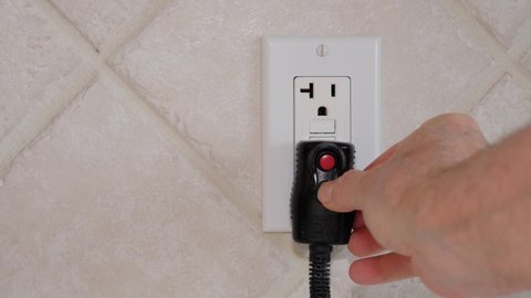 Close up of male hand inserting cord with GFI plug into electricity receptacle. Residential ground fault interrupter electric socket plug and wall plate.