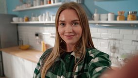 Happy teen girl talking to the camera holding a phone recording vlog. blonde woman influencer social media streaming, video calling in online chat using smartphone at home. Mobile cam horizontal view Kitchen.