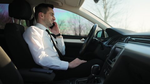 Handsome man driver speaking on phone, having conversation using smartphone. Young Businessman Talking On Mobile Phone In A Car. Lifestyle, road, car concept.
