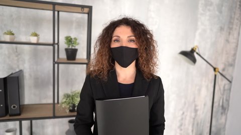 Focused business woman in disposable black face mask holds a folder with documents in his hands in office. Preventions of viral infection spread. New rules during the COVID-19 pandemic
