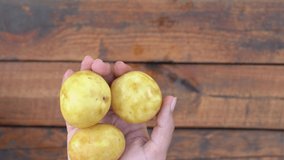Closeup top view 4k stock video footage of woman peeling young fresh raw potatoes isolated at blurry brown wooden table background