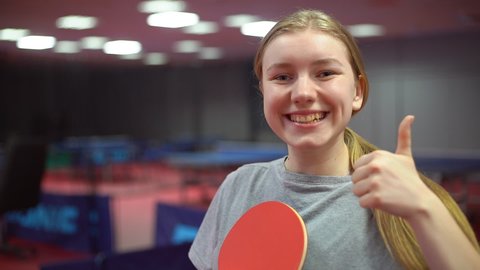 Portrait of a smiling teen girl table tennis player with a ping pong racket. Thumb up