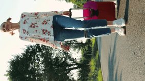 From below shot of young female smiling and pulling red suitcase while walking on asphalt road during trip through countryside. Video with Vertical Screen Orientation 9:16