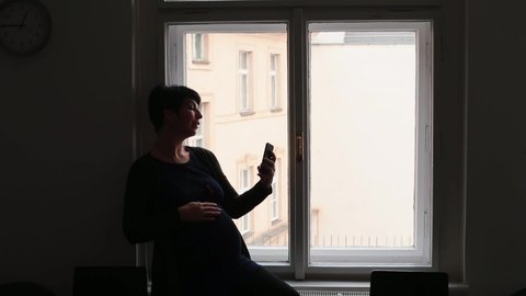 Waiting planned caesarean section hospital, mental stress relief. Woman makes selfie using smartphone window. Dark room inside light buildings outside. Using phone Cz, Prague, Myslikova, 23.12.2020. 