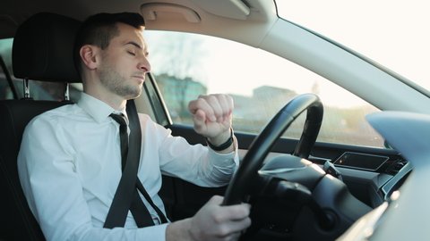 Businessman using smart watch on his hands while driving a car, urban background, technology innovation. Concentrated man sitting at driver's seat in car.