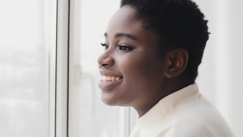 Portrait of afro american girl ethnic black woman female profile looking out window, standing in daylight, enjoying view, dreaming about future plans, smiling contemplating in morning at home indoors | Shutterstock HD Video #1069700440