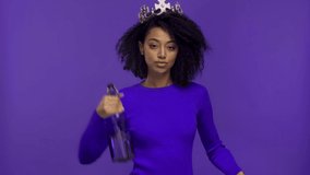 smiling african american woman dancing with bottles isolated on purple