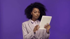 thoughtful african american businesswoman using digital tablet isolated on purple