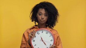 smiling african american woman dancing with clock isolated on yellow