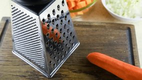 Cream of roasted pumpkin soup recipe. Step 9. Male person grates orange carrot on a grater standing on wooden cutting board. Point of view. 4k resolution video. Home cooking theme.