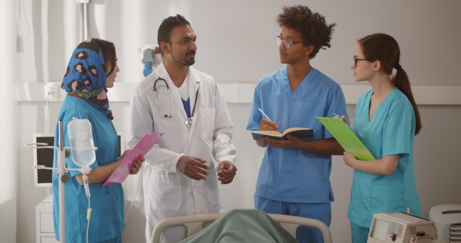 Mature indian doctor giving lecture to interns in hospital ward discussing patient diagnosis. Team of multiethnic medical students during internship in modern clinic | Shutterstock HD Video #1069707592
