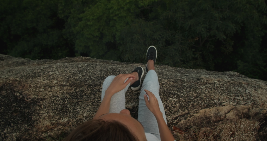 View from above to behing of girl sitting on rock cliff ad overlooking landscape sea view