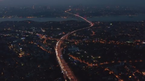 Highway Freeway Road going through Istanbul City with Red Illuminated Bosphorus Bridge in the distance at Night, Aerial Wide View