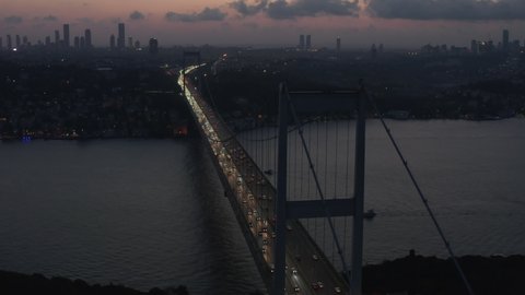 Istanbul 15 July Martyrs Bosphorus Bridge at Dusk or Night with City Skyline Silhouette and Car traffic flowing out of the City lights, Aerial slide right