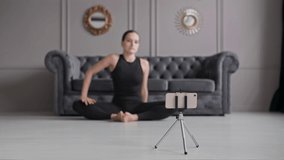 Woman blogger recording stretching exercise at phone. Female practicing yoga at home. Focus on smartphone. Brunette woman streaming online training. Healthy lifestyle at quarantine. Social distance